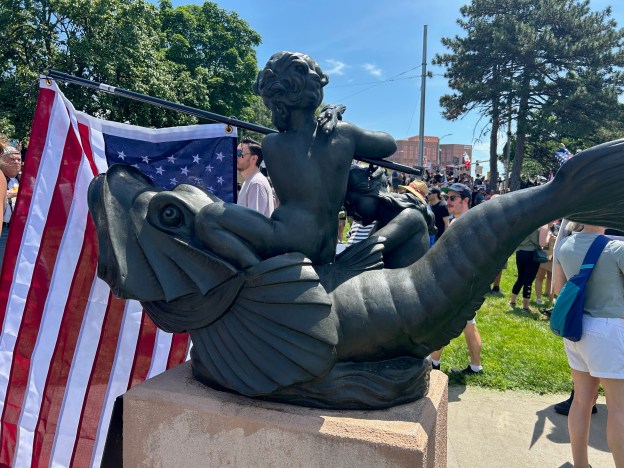A statue of a water spirit with an American flag in distress in its arms